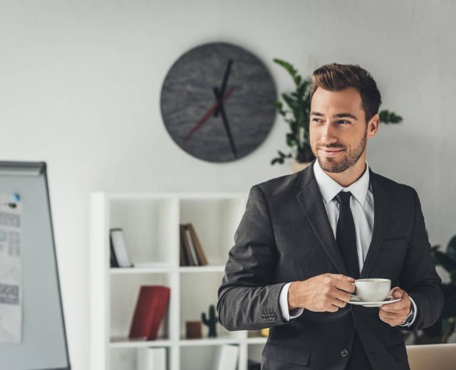 happy-young-businessman-with-cup-of-coffee-at-offi-2021-08-31-22-17-08-utc.jpg